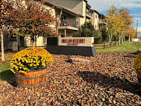 Property entrance sign with yellow mums in barrel planter at Mullan Reserve Apartments, Missoula