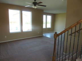 an empty living room with a ceiling fan and a staircase