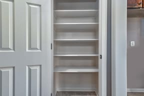 a walk in closet with white shelves and a door