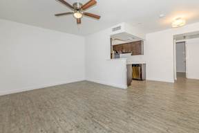 A room with a ceiling fan and a kitchenette in the background.