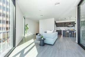 A modern living room with a white couch and a kitchen area in the background.