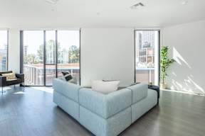 A light blue couch with a white pillow is in the middle of a room with a balcony outside.