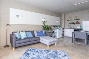 A grey couch with blue pillows sits in a room with a white wall and a blue rug.