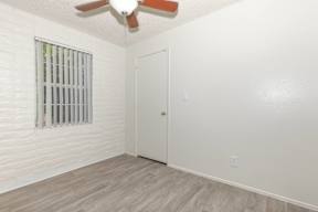A room with a white door, a window with bars, and a ceiling fan.