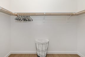 A white wall with a clothes rack and a waste basket.