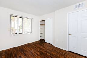A room with a white door, a window with blinds, and a wooden floor.