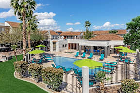 A pool area with a green umbrella and blue chairs.