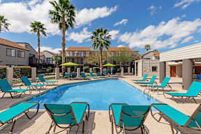 A pool surrounded by lounge chairs and palm trees.