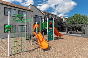 A playground with a green ladder, a green and orange slide, and a green and orange climbing structure.