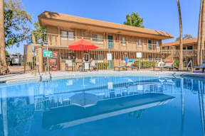 A swimming pool in front of a building with a red umbrella.