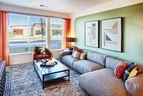 A living room with a grey couch, a glass coffee table, and two framed artworks on the wall.