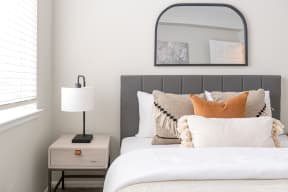 a bedroom with a bed and a nightstand with a lamp and a mirror above it