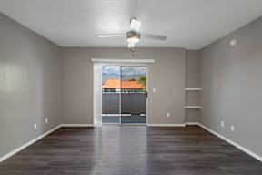 A room with a ceiling fan and a view of a fence and a building outside the window.
