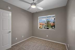 A room with a ceiling fan and a window showing a view of a house.