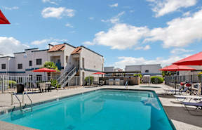 A swimming pool in front of a building with red umbrellas.