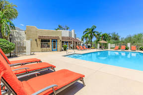 A pool with red sun loungers and a building in the background.