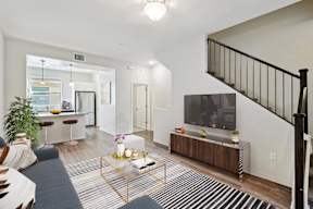 A living room with a black and white striped rug, a wooden coffee table, a TV, and a staircase with a black railing.