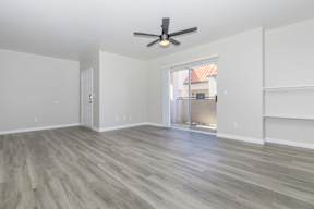 A room with a ceiling fan and light, hardwood floors, and a sliding glass door leading to a balcony.