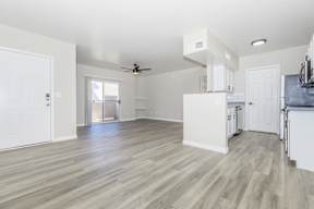 A spacious kitchen and living room with white walls and wood flooring.