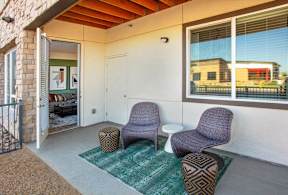 A patio with two chairs and ottoman with a green rug.