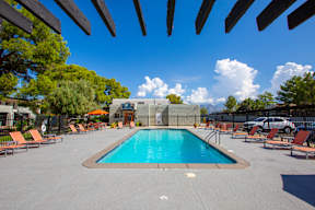 A large swimming pool surrounded by orange lounge chairs and wooden pergolas.