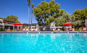 A swimming pool surrounded by trees and chairs with umbrellas.