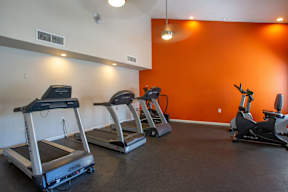 A gym with orange walls and treadmills.