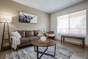 A living room with a brown leather couch, a coffee table, and a painting of a cow on the wall.