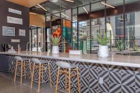 A modern bar with a white counter and wooden stools.