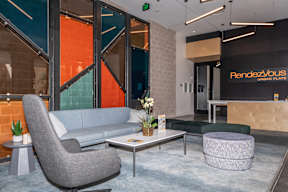 A grey chair is in front of a glass wall with a sign that says "Rendezvous Urban Flats".