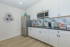 A kitchen with white cabinets and a grey fridge.