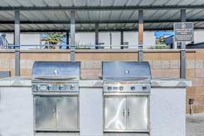 Two stainless steel BBQ grills are on a patio.