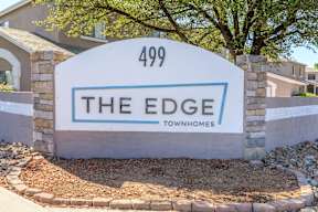A sign for "The Edge" townhomes stands in front of a building.
