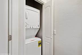 A white fridge is in a narrow space between a door and a wall.