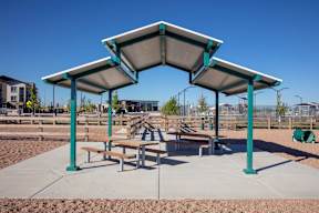 A playground with a shelter and benches is set in a sandy area.