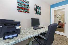 A black computer monitor sits on a desk with a black chair.