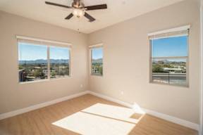 A room with a ceiling fan and two windows overlooking a landscape.