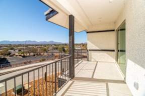 A balcony with a metal railing overlooks a parking lot and distant mountains.