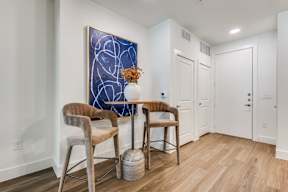 A blue abstract painting hangs on a white wall above a table with two chairs.