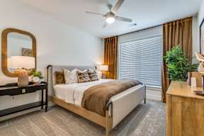 A bedroom with a bed, a mirror, a nightstand, and a plant.
