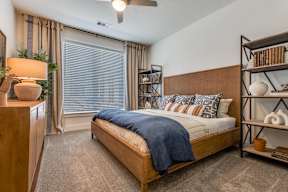 A bedroom with a bed, a nightstand, and a window with blinds.