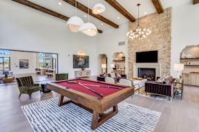 A pool table is in the middle of a room with a stone fireplace and a TV.