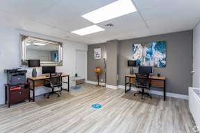 A room with two desks and a printer on a cabinet.