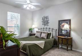 A bedroom with a bed, a ceiling fan, and a painting of a sunflower.