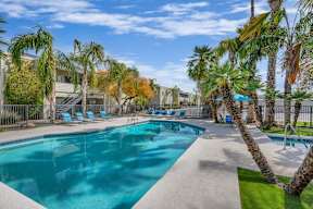 A swimming pool surrounded by palm trees and lounge chairs.