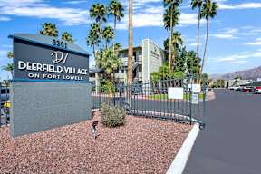 A sign for Deerfield Village on Fort Lowell stands in front of a building and palm trees.