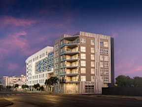 A modern apartment building with a glass facade stands tall against a twilight sky.