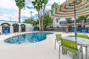 A pool with a table and chairs and a striped umbrella.at Icon Apartments, Arizona, 85712