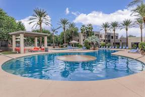 A large swimming pool surrounded by palm trees and a pavilion.