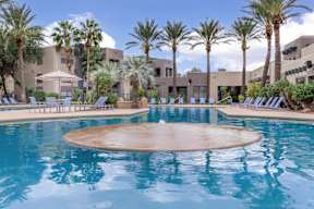 A large outdoor swimming pool surrounded by palm trees and lounge chairs.